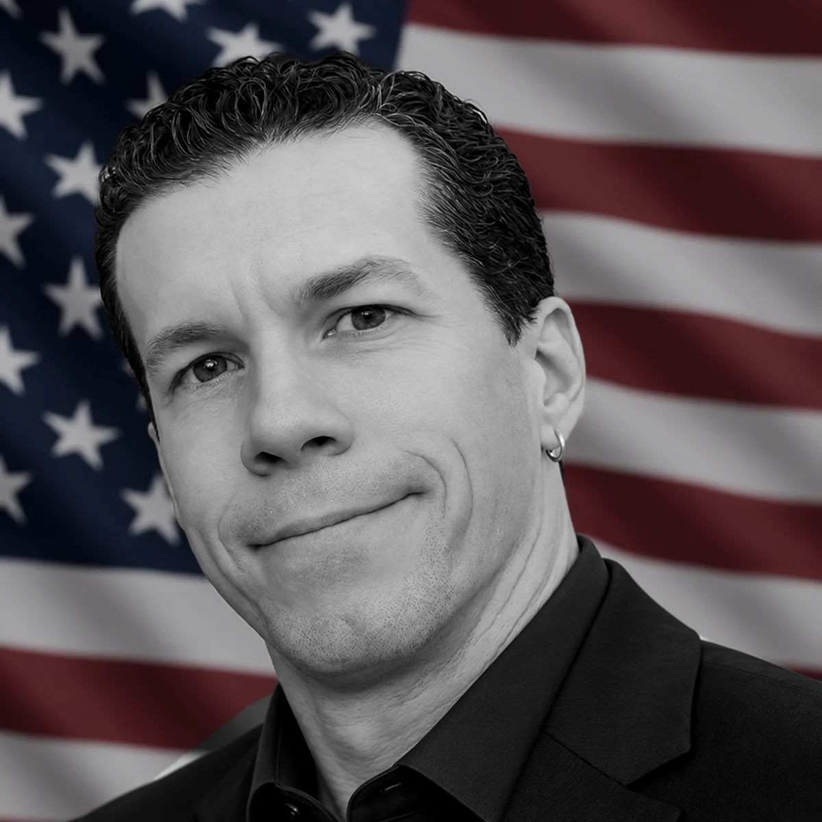 Brian W. Smith, smiling, in a dark jacket in front of a United States flag